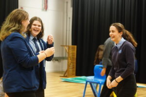 School children in a drama studio with black curtains creating a tableau and smiling